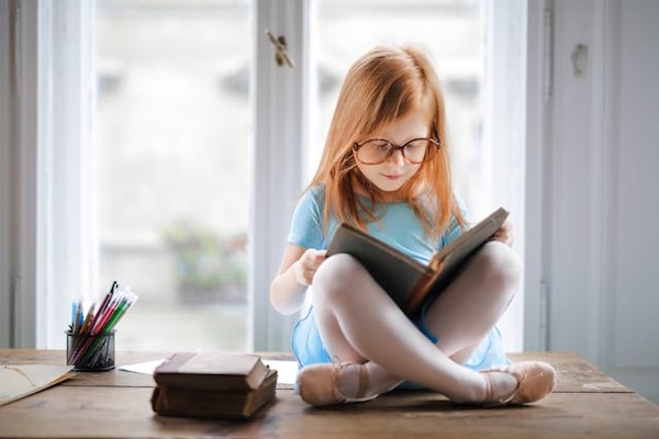 enfant lisant un livre et portant des lunettes